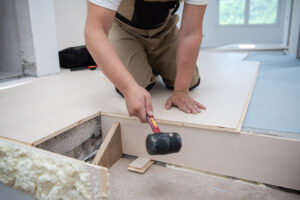 professional carpenter using rubber hammer while installing new laminated wooden floor in a unfinished apartment