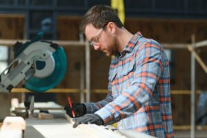 Wood cutting table with electric circular saw. Professional carpenter in uniform cutting wooden board at sawmill carpentry manufacturing . Sawing machine.